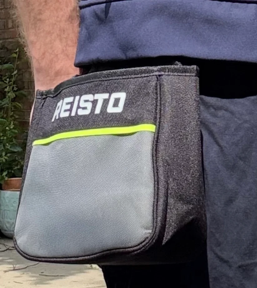 Close-up of the Reisto cartridge pouch worn at the waist, featuring black and grey fabric with fluorescent yellow trim and white REISTO branding.